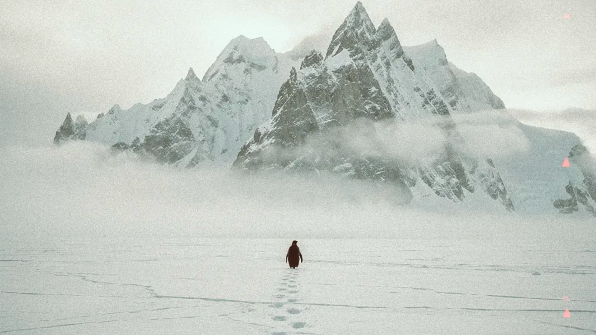A lone penguin walking across a vast icy landscape toward towering snow-covered mountains